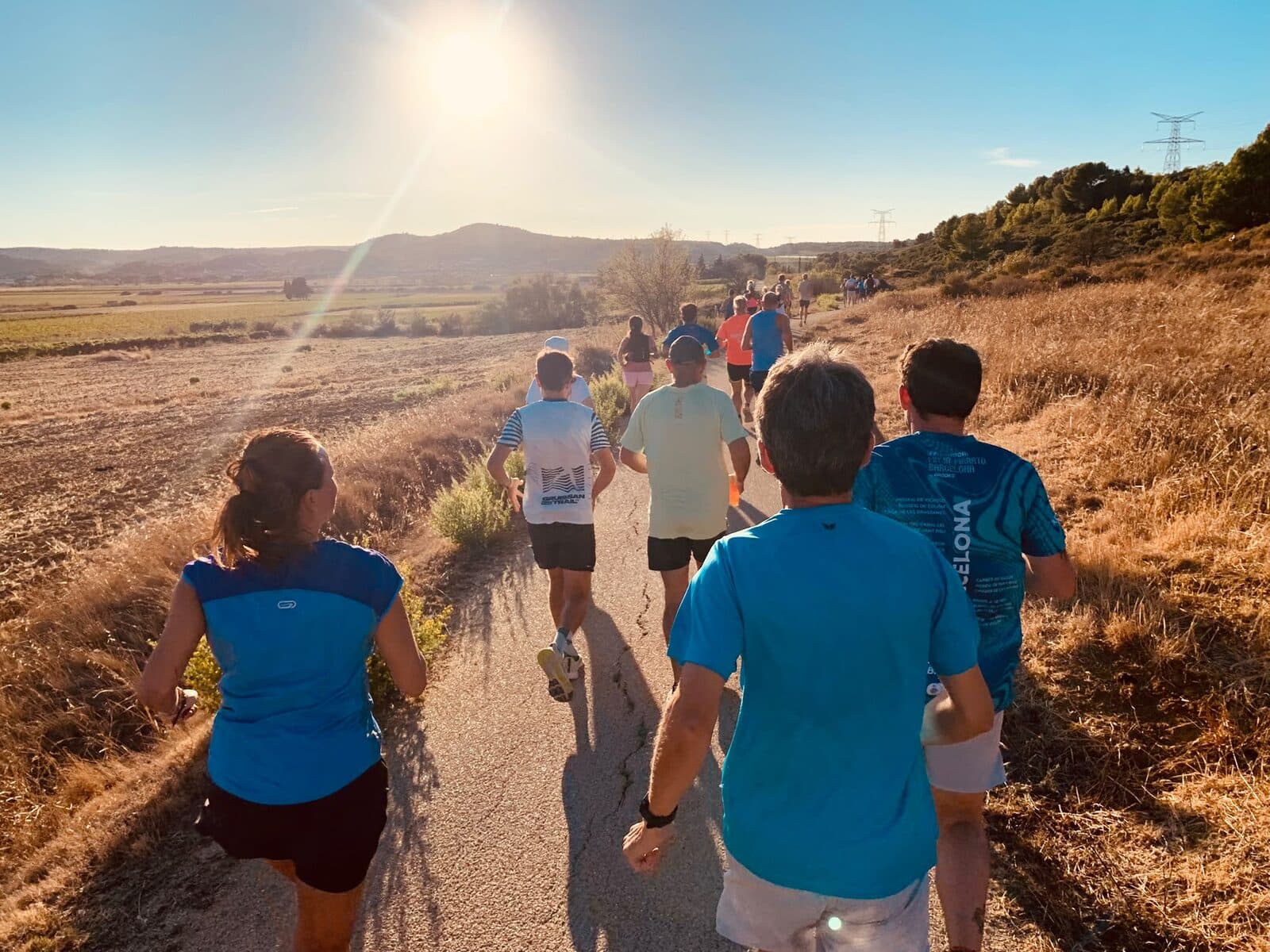 Des coureurs de dos sur une petite route de campagne, face au soleil couchant