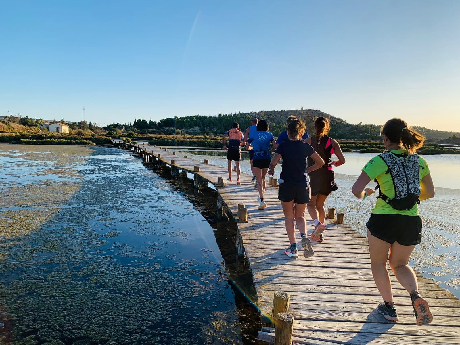 Des coureurs du club en file sur une passerelle en bois au-dessus de l'étang, au soleil du matin