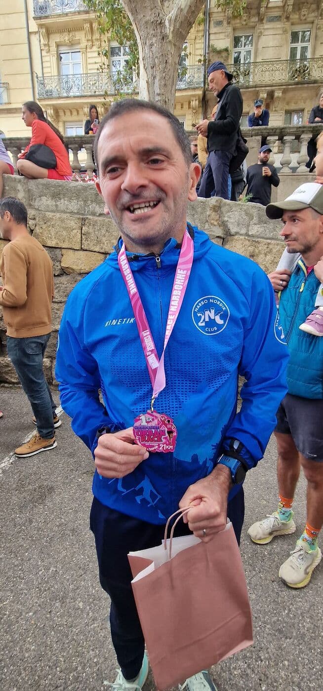 Un coureur du Narbo Nordik Club en veste bleue montre sa médaille rose de finisher
