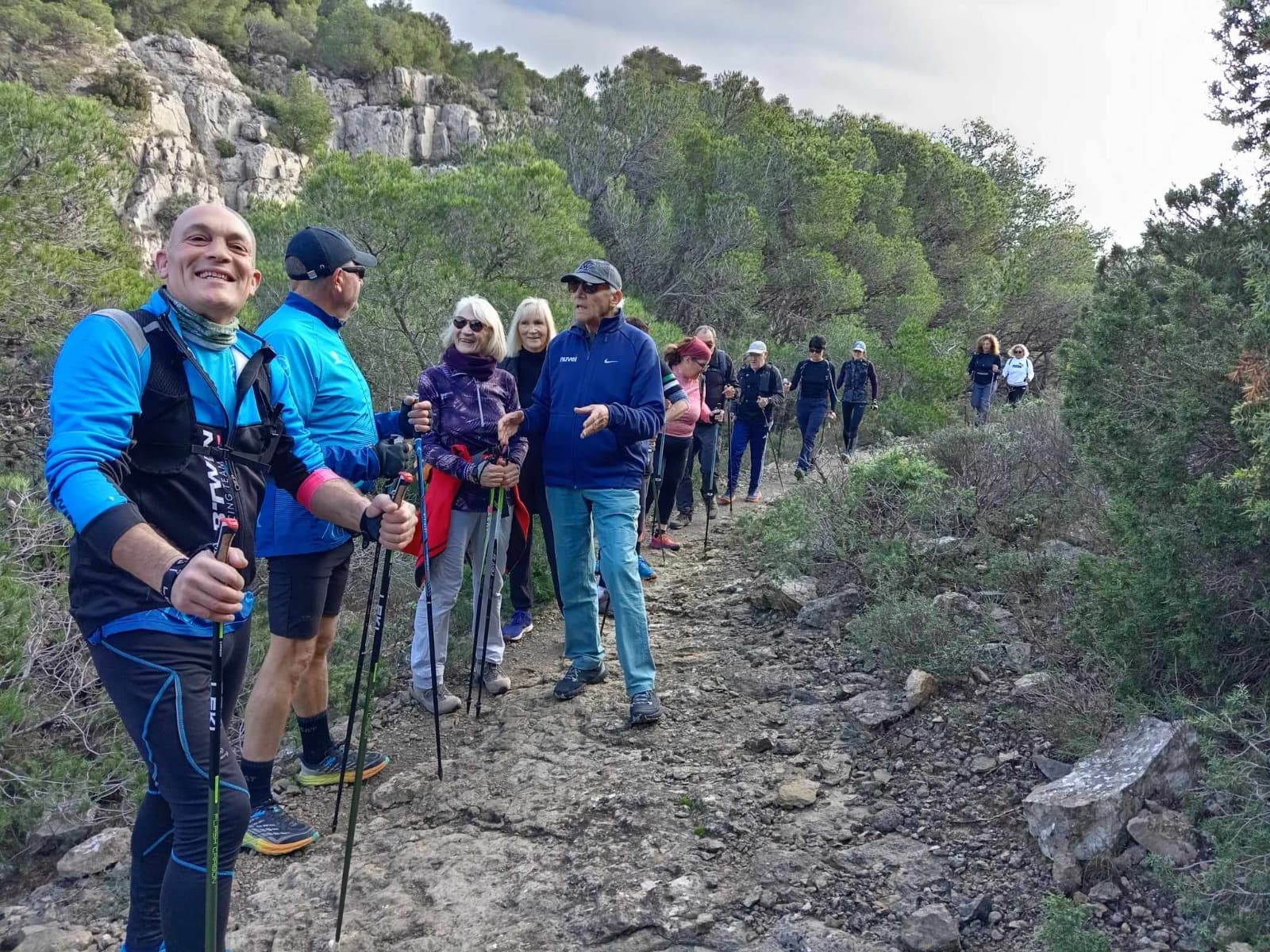 Groupe de marche nordique du club en file sur un sentier de garrigue, sous les falaises